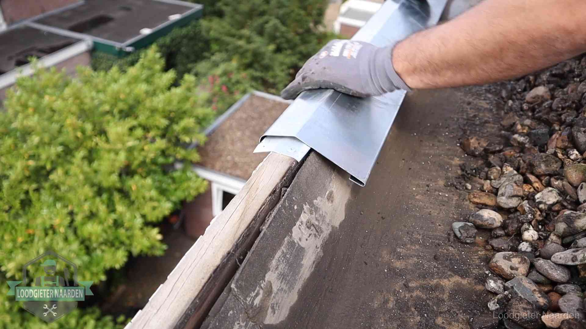 Daklekkage per wijk in Naarden Dakdekker plaatst een zinken deklijst op een dakrand met uitzicht over een woonwijk in Naarden