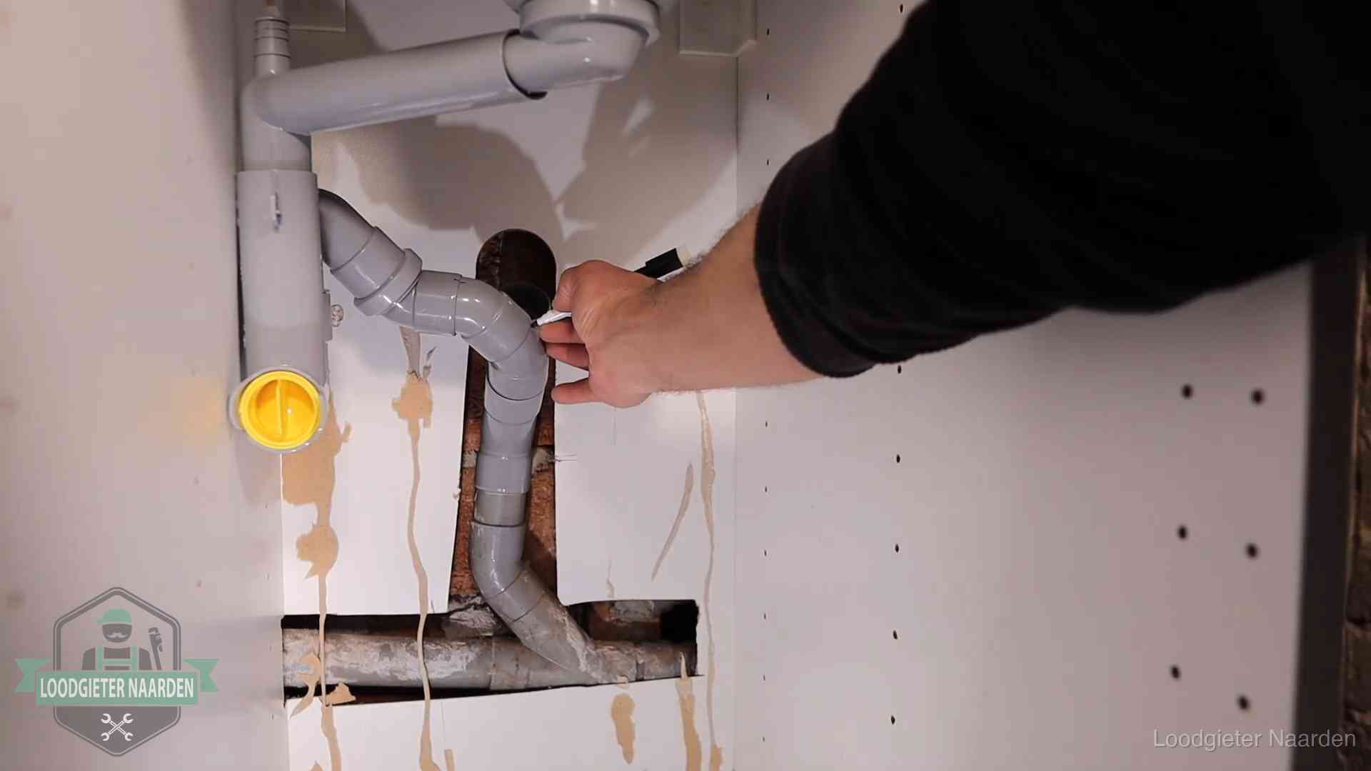 Loodgieter voor verhuurders en bedrijven in Naarden Loodgieter markeert een pvc-afvoerbuis onder een gootsteen in Naarden