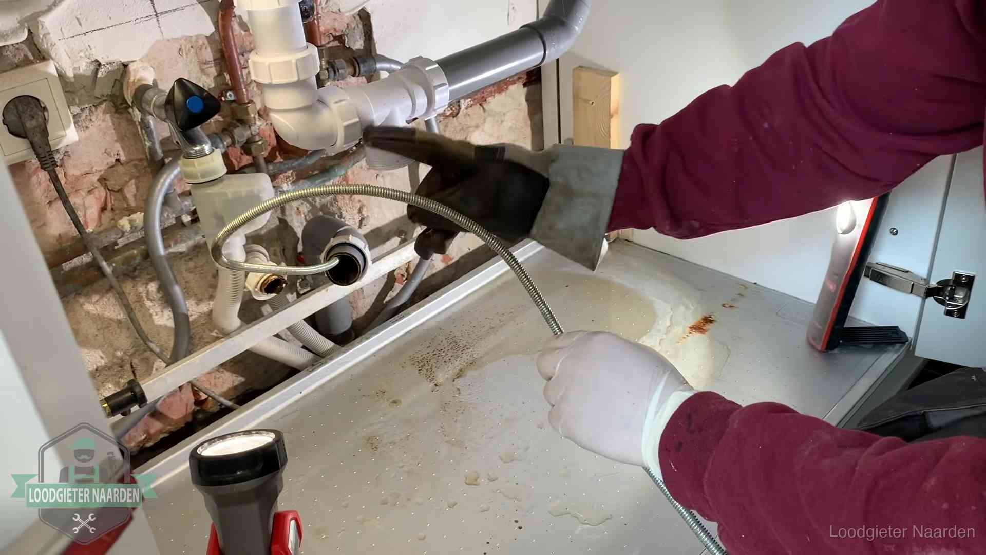 Ontstoppingsveer gaat in een geopende sifonaansluiting onder het aanrecht in Naarden