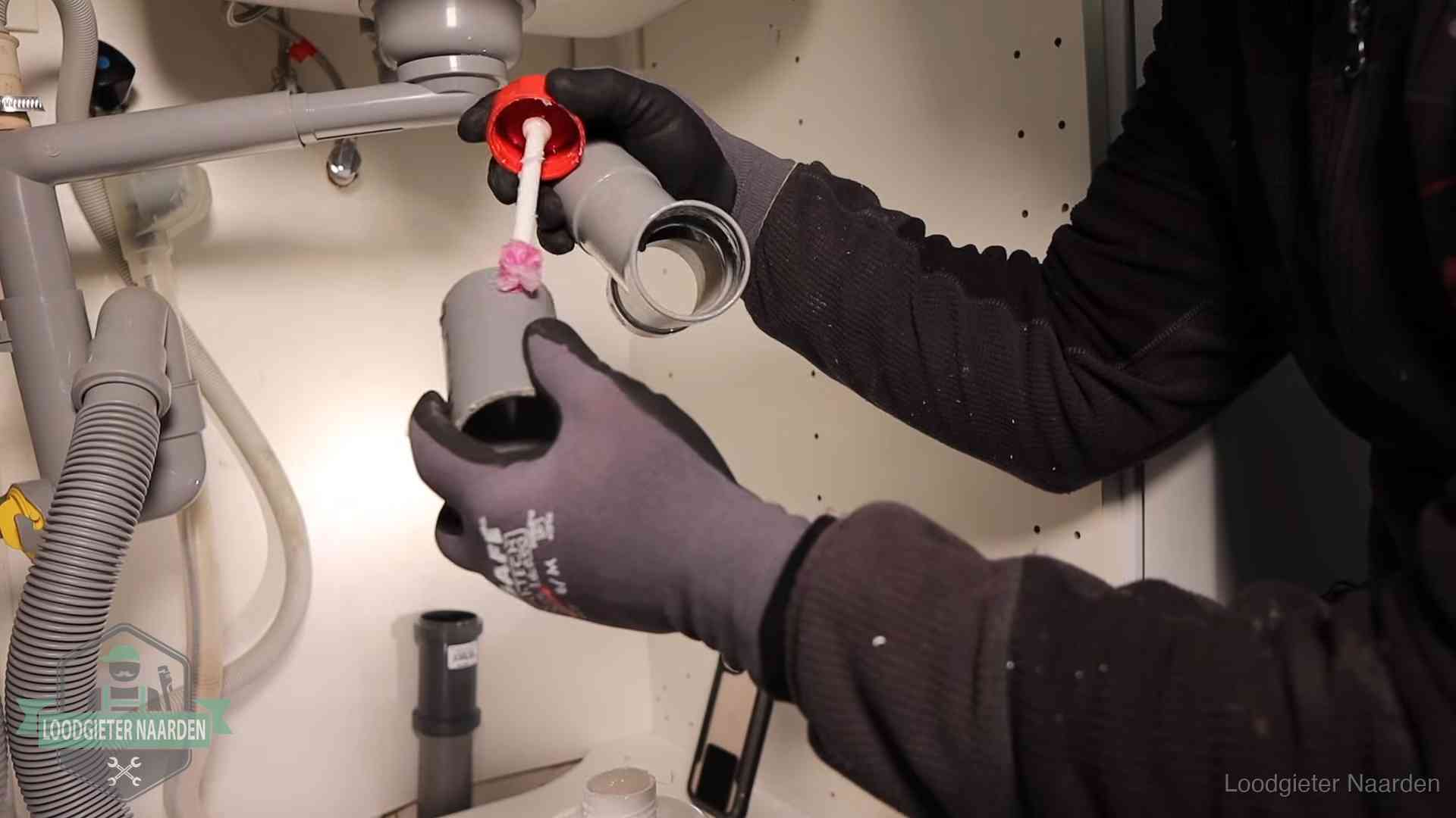 Loodgieter demonteert en reinigt de sifon onder een keukenkast in Naarden