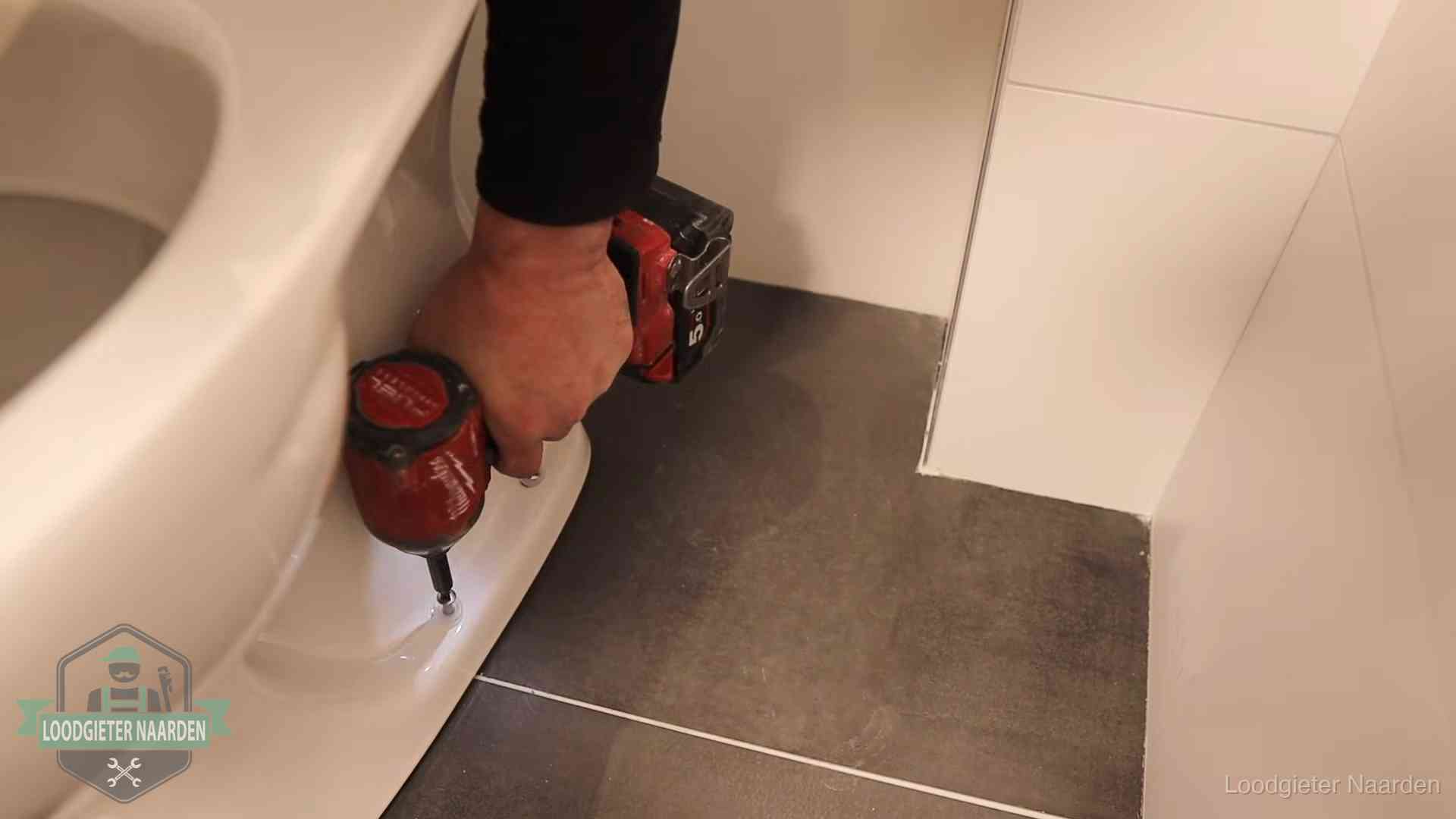 Loodgieter zet de voet van een wc-pot vast op de tegelvloer in Naarden